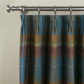 A rich wool plaid curtain in blue teal gold and earthy brown tones with pencil pleats hanging from a brushed nickel rod and rings