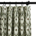 Close-up of an off-white pleated curtain with a repeating pattern of dark red roses and green leaves forming a diamond garland design hanging from a black rod with black rings