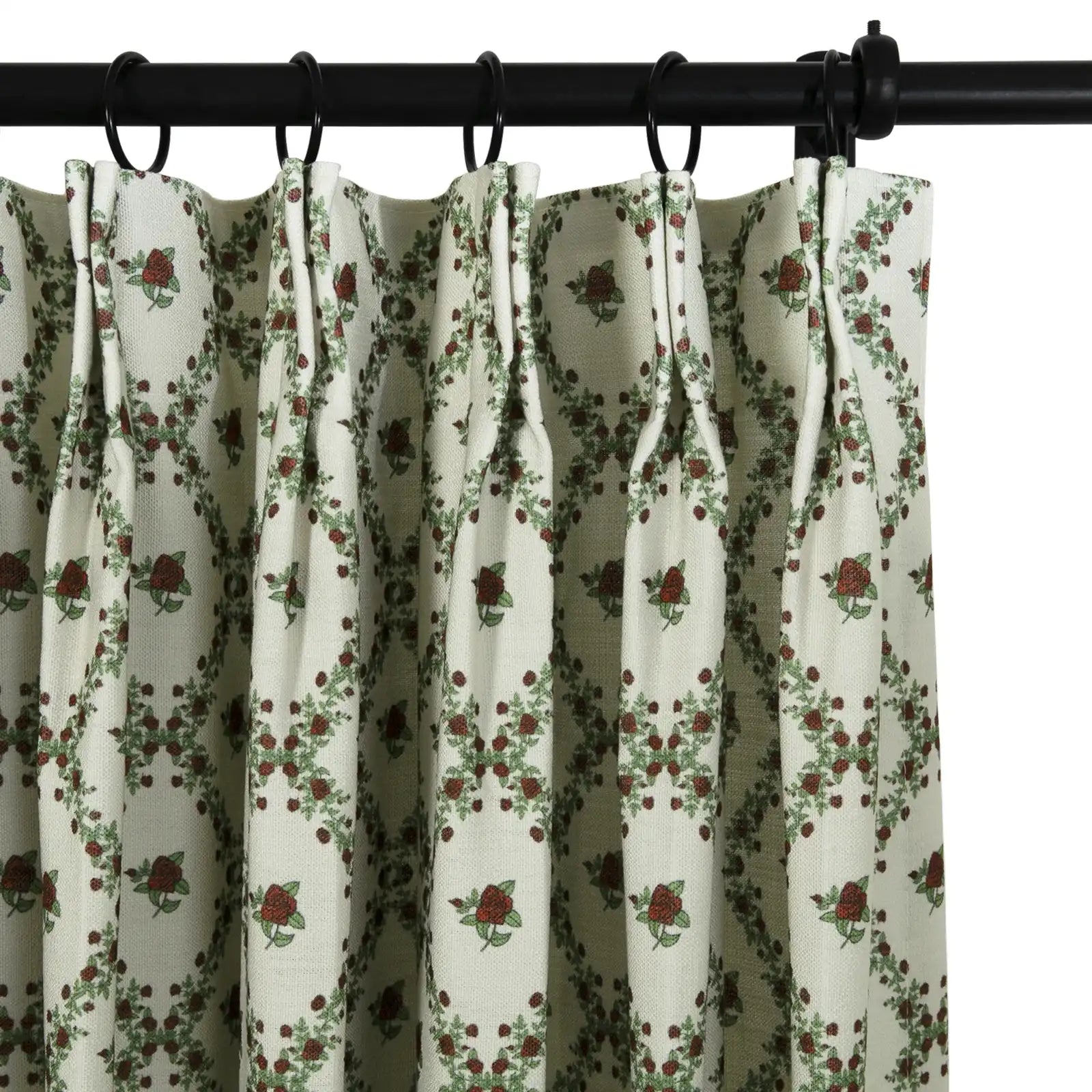 Close-up of an off-white pleated curtain with a repeating pattern of dark red roses and green leaves forming a diamond garland design hanging from a black rod with black rings
