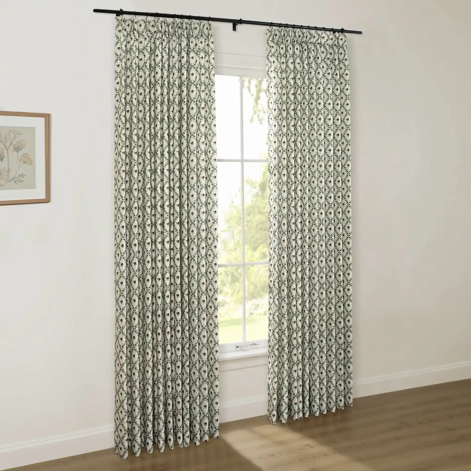 Interior room with light walls and a wooden floor showcasing pleated off-white curtains featuring a dark green diamond trellis pattern with small red floral motifs, hung from a black rod over a window, alongside a framed botanical print on the left wall