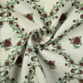 Woven fabric featuring a repeating pattern of dark red roses and green leaves on a cream background with a subtle textured weave and soft fabric folds