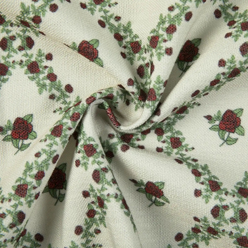 Woven fabric featuring a repeating pattern of dark red roses and green leaves on a cream background with a subtle textured weave and soft fabric folds
