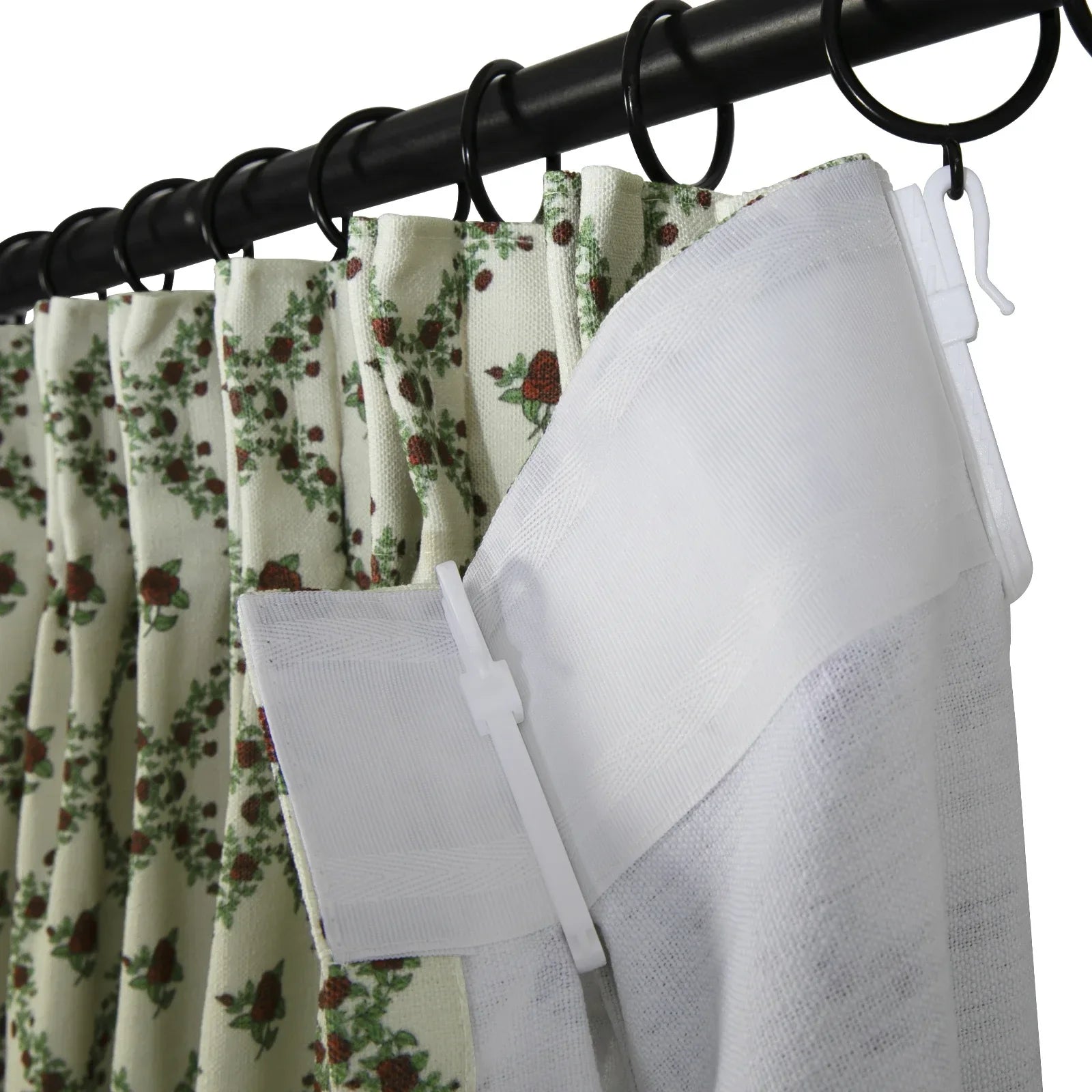 Cream curtains with a reddish-brown rose and green leaf floral pattern hanging from a black curtain rod with black rings, revealing a white back tab hook system