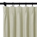 Photograph of a textured light oat-colored curtain with distinct pleats hanging from a black rod and matching rings