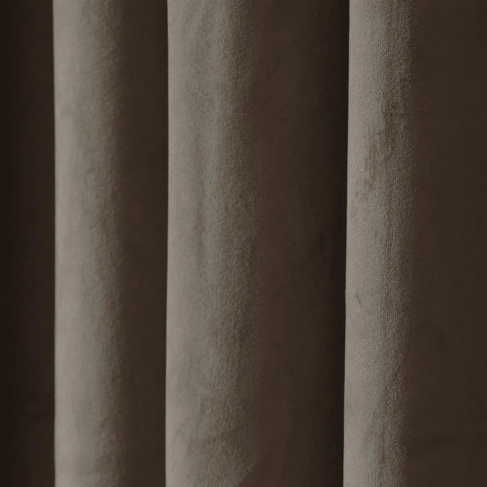 Close-up of pleated taupe velvet fabric showcasing its soft texture and dynamic light and shadow across vertical folds