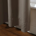 A close-up view of a flowing taupe curtain with a neat hemline next to a warm wooden floor and sunlit white window trim