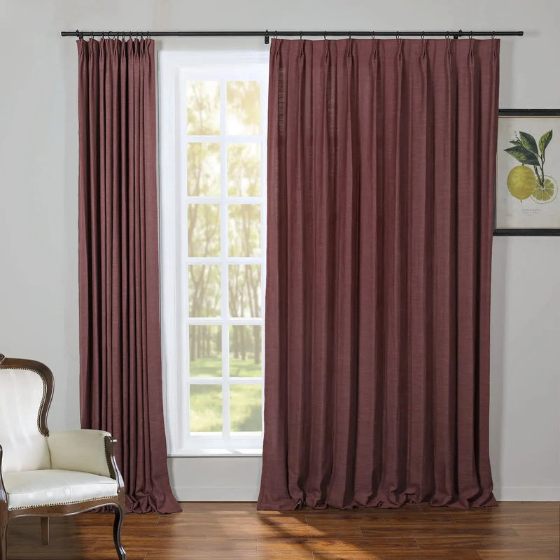 Deep maroon pinch pleat curtains frame a white grid window in an interior room, complemented by a classic white upholstered armchair and a framed lemon botanical print
