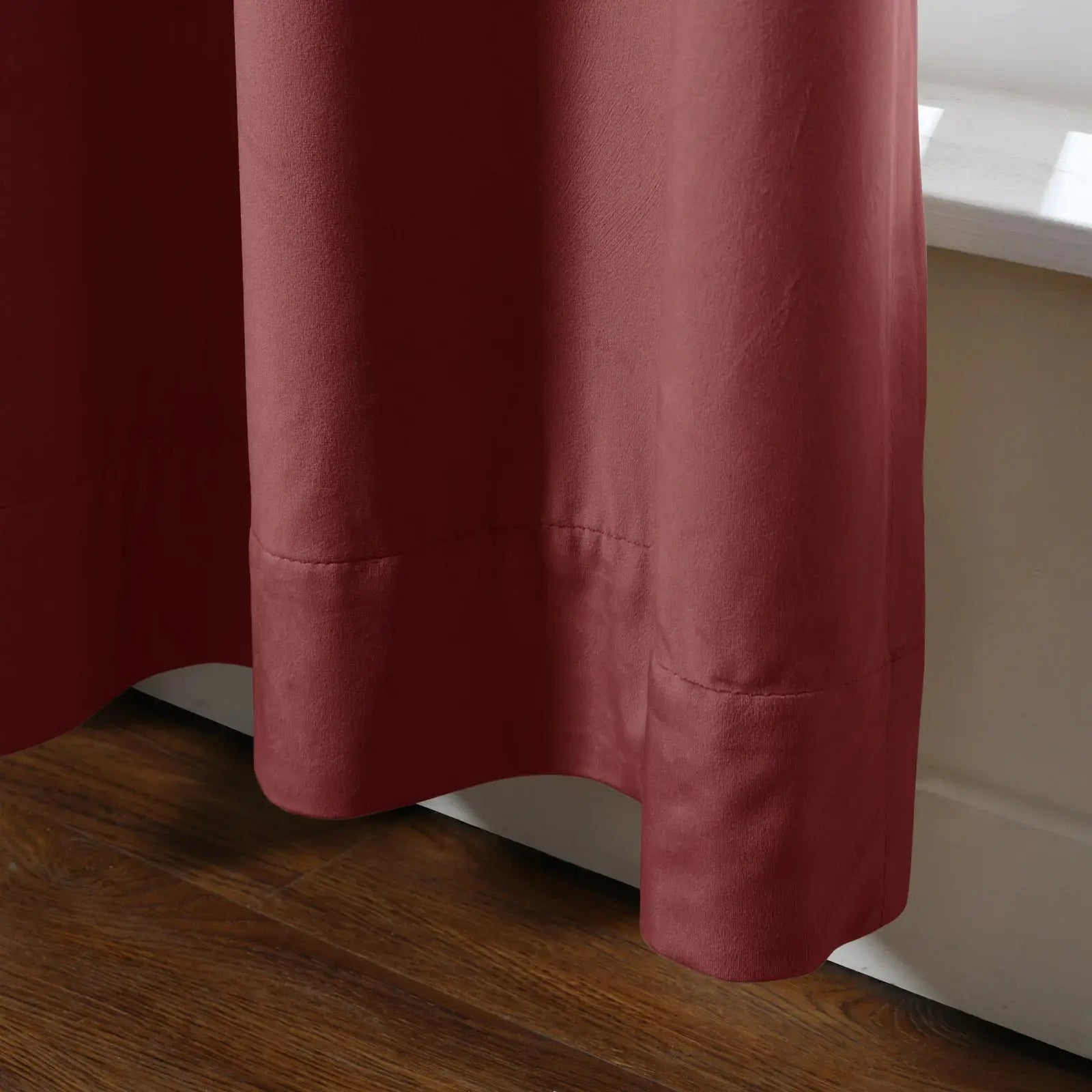 A single terracotta drapery panel featuring subtle vertical folds and a visible stitched hem resting above a light window sill and dark wood floor