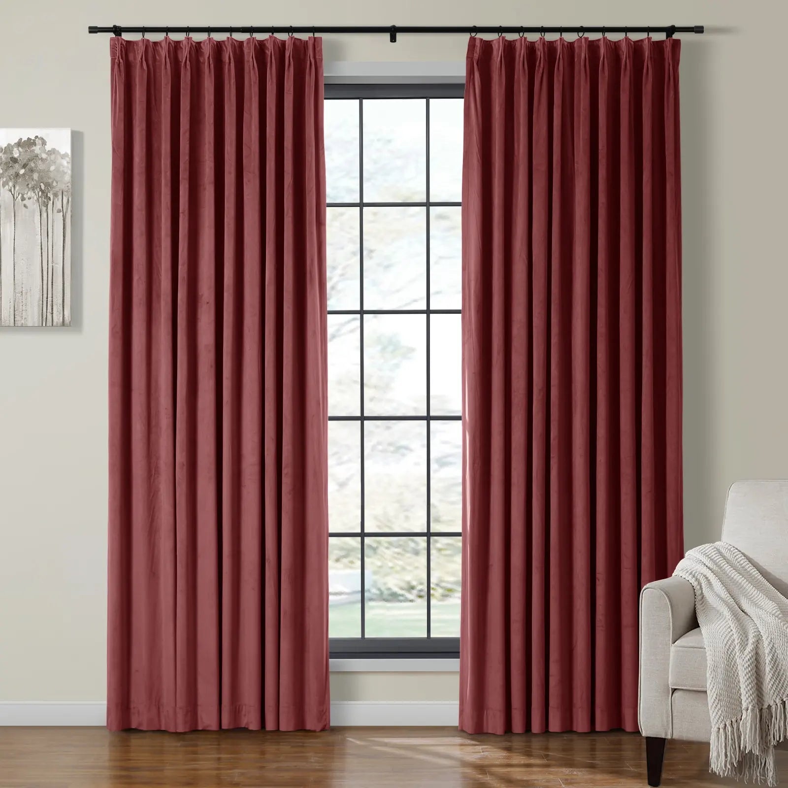 Deep red velvet pleated curtains on a black rod frame a large window with black grid panes in a room also showing a modern gray tree artwork and a neutral armchair with a white textured throw