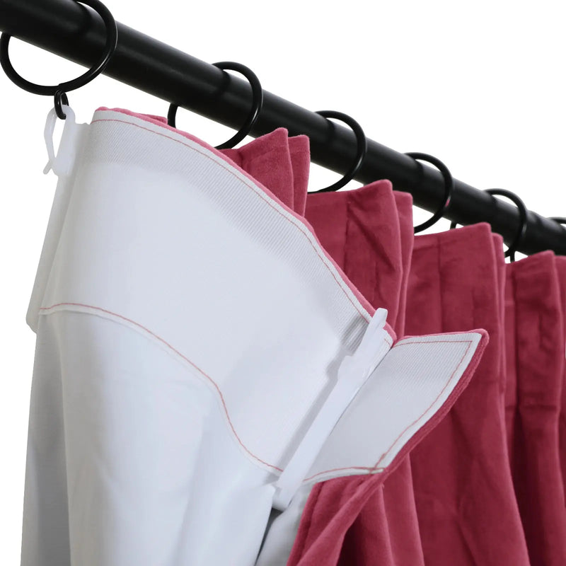 Close-up showing a pleated dark pink velvet curtain with a white liner and red stitching connected by white plastic hooks to a black metal curtain rod with matching black rings against a plain white background