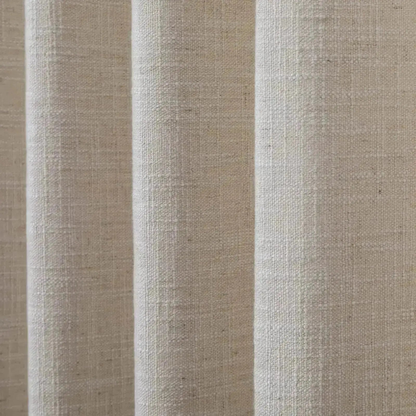 A close-up photograph of natural light beige textured fabric showing visible vertical folds and a coarse weave
