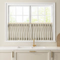 A modern kitchen featuring a window with pleated striped cafe curtains on a brass rod above a white double sink with a sleek gold faucet set into a white quartz countertop