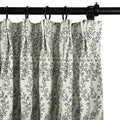 Photograph of a light green pleated curtain featuring a dark gray leafy branch pattern, suspended by black rings from a black curtain rod