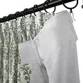 Black curtain rod with rings holding a pleated white curtain featuring a dark green botanical leaf pattern and a solid white textured curtain panel with a herringbone weave joined by a white plastic clip