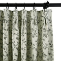 Fabric pleated curtain in light beige featuring a dark grey floral vine pattern hanging from a black curtain rod with black rings