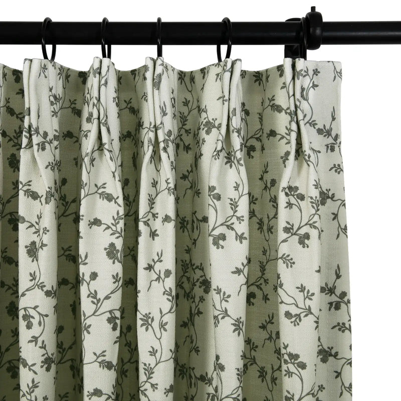 Fabric pleated curtain in light beige featuring a dark grey floral vine pattern hanging from a black curtain rod with black rings