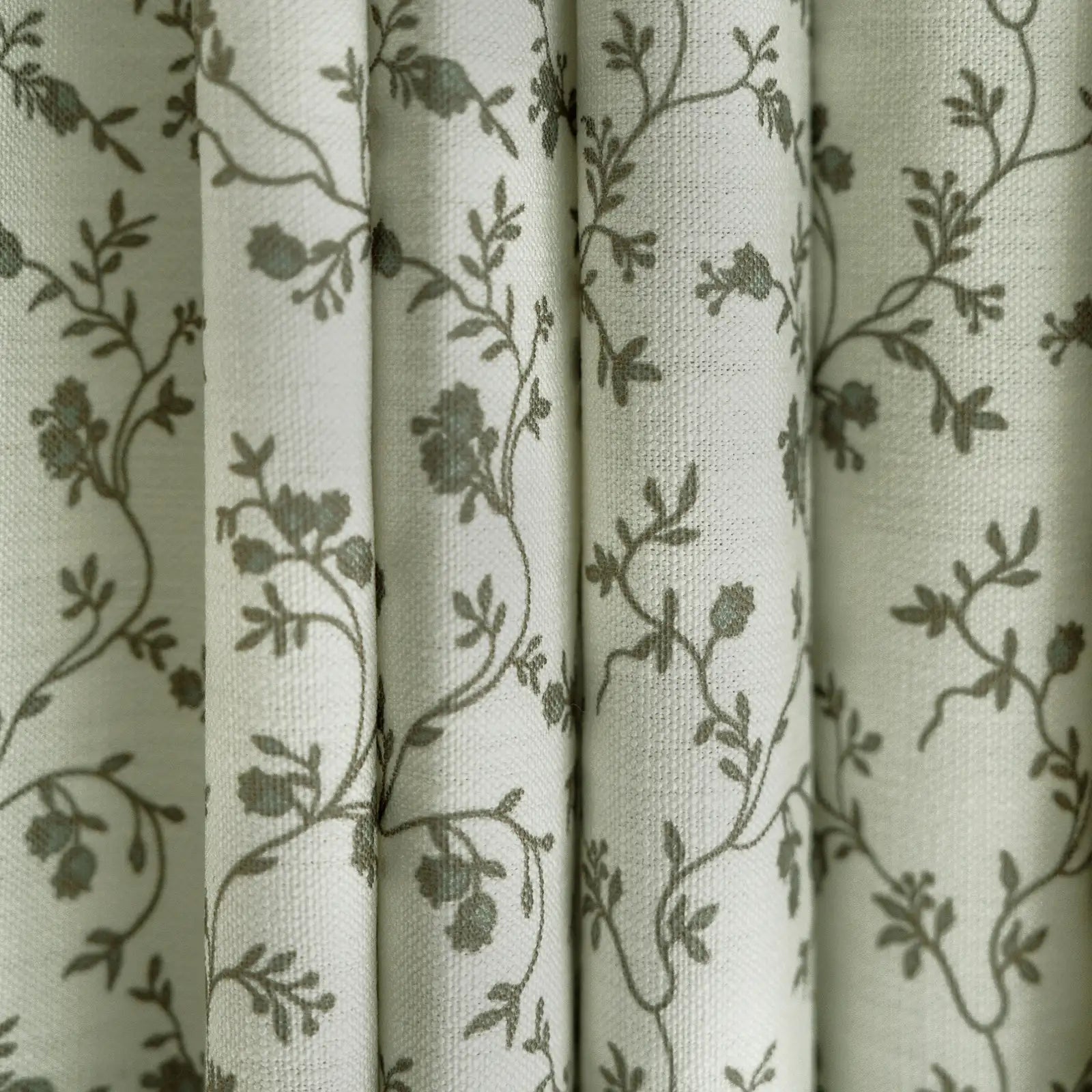 Textile patterned curtains featuring an off-white background with delicate gray-green floral vine motifs and a visible woven texture