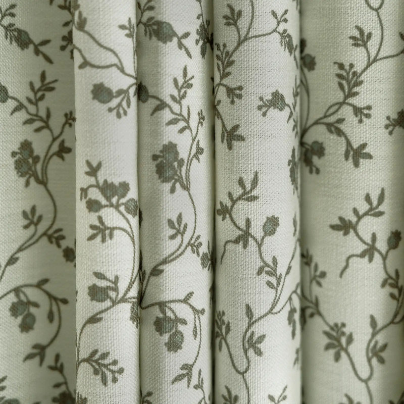 Textile patterned curtains featuring an off-white background with delicate gray-green floral vine motifs and a visible woven texture