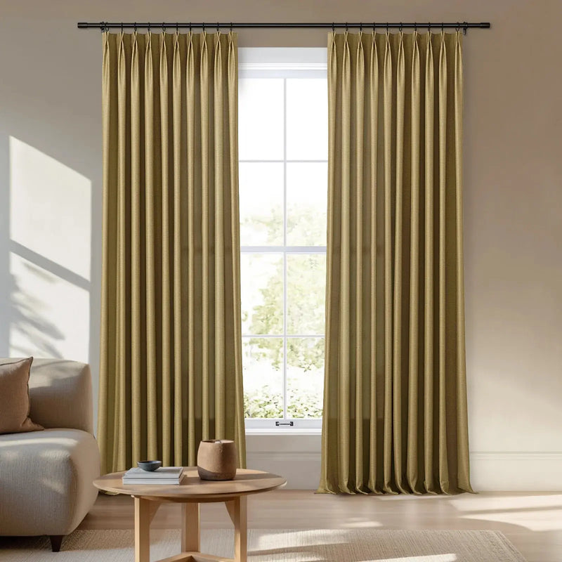 Photography of pleated olive gold curtains on a black rod framing a four-pane window in a bright modern living room featuring a cream sofa and a round wooden coffee table casting sunlit shadows