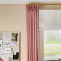 Interior view of a pink wall with a mood board displaying design swatches and paper cat chains beside a window featuring a pink pinch-pleat curtain on a gold rod and a white Roman blind overlooking a green backyard with a small grey shed