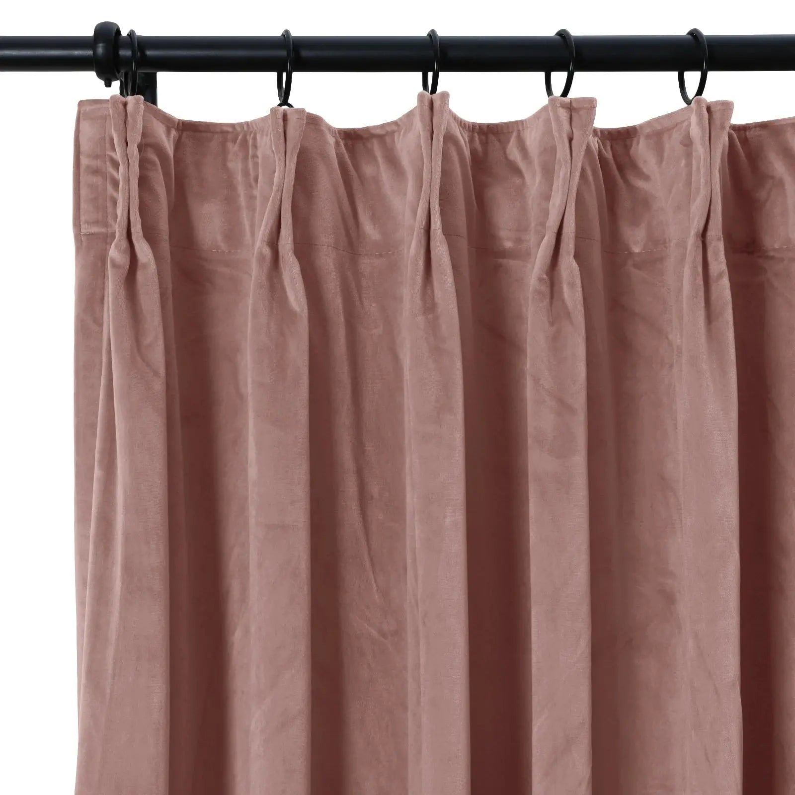 Photograph of a dusty rose velvet pinch pleat curtain hanging from a black metal rod with rings