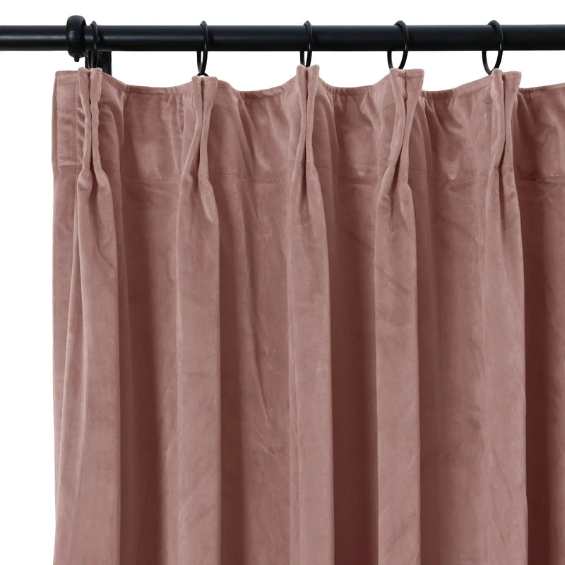 Photograph of a dusty rose velvet pinch pleat curtain hanging from a black metal rod with rings