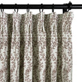 Textile image of an off-white pleated curtain adorned with a dense brown leafy vine pattern, suspended by black rings on a dark metal rod