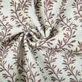 Textile photograph of cream woven fabric featuring a repeating brown vine and leaf pattern with soft folds and a central swirl