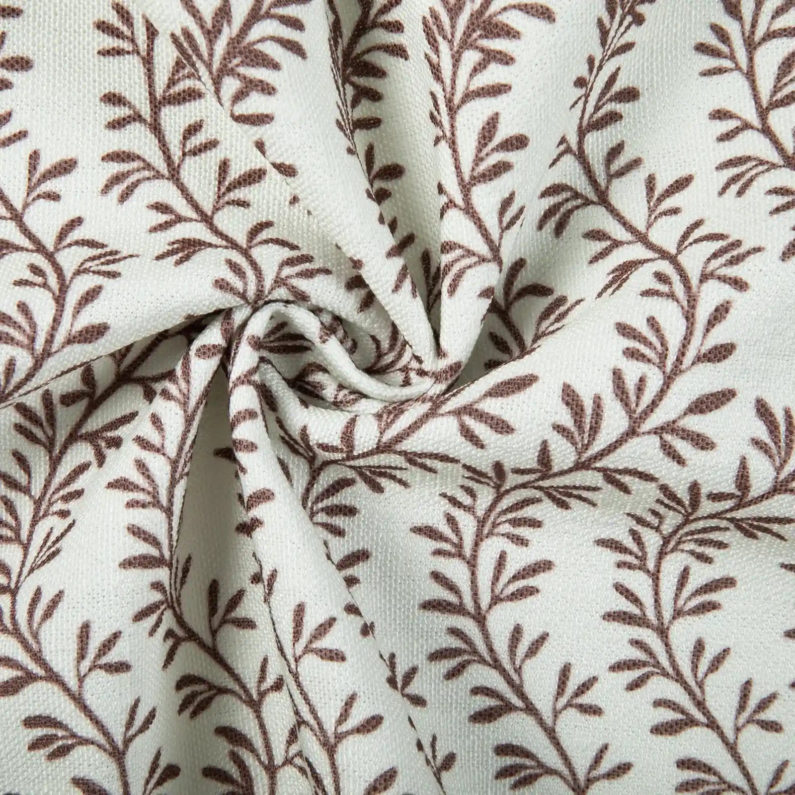 Textile photograph of cream woven fabric featuring a repeating brown vine and leaf pattern with soft folds and a central swirl