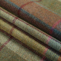 Photograph of folded tweed fabric with a herringbone weave displaying an earthy plaid pattern featuring prominent lines of muted blue, deep red, and olive green