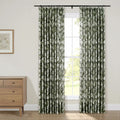 Pleated dark green and white floral curtains on a black rod framing a window, beside a light wood mid-century modern dresser and framed botanical print on a cream wall