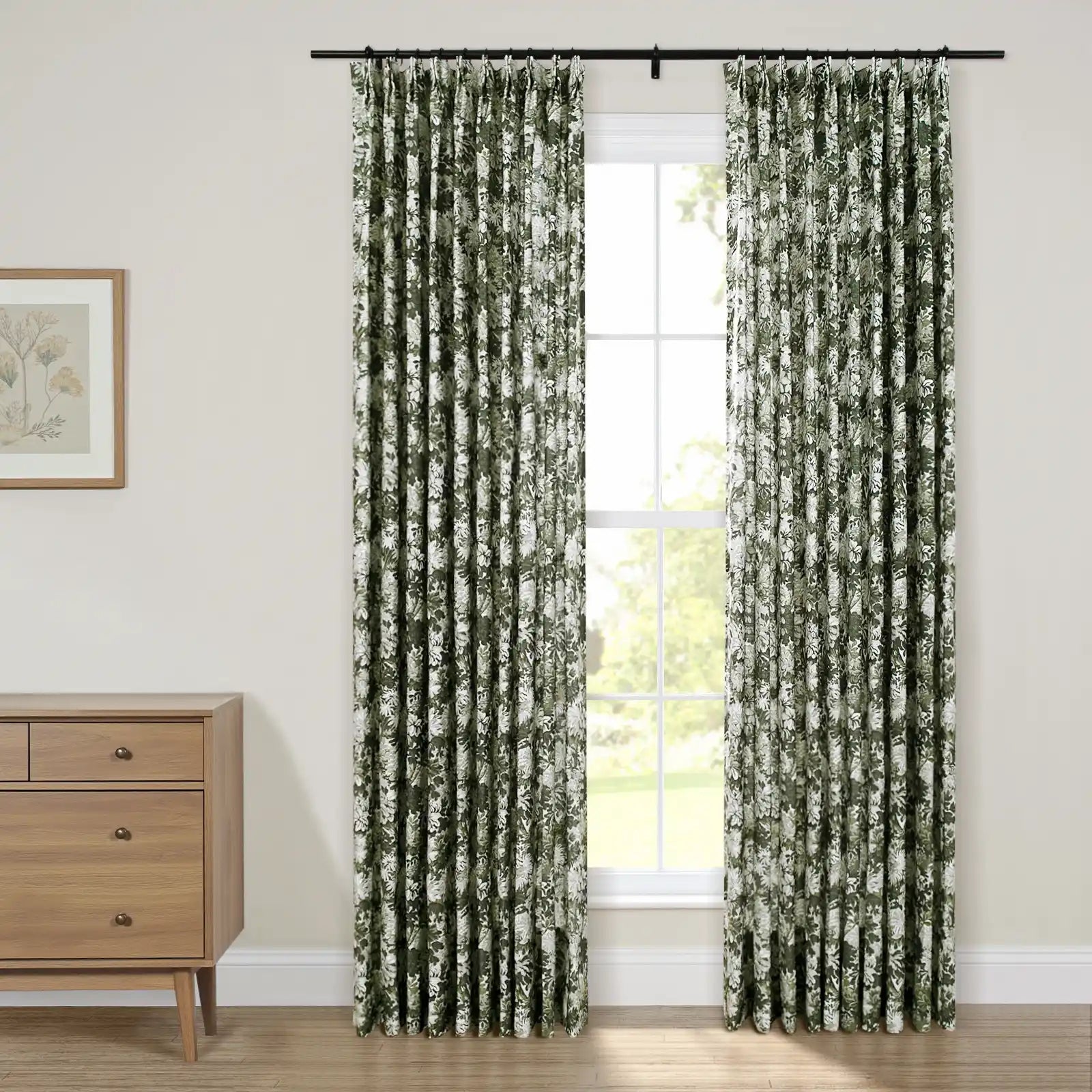 Pleated dark green and white floral curtains on a black rod framing a window, beside a light wood mid-century modern dresser and framed botanical print on a cream wall