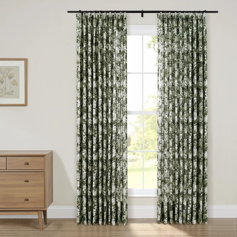 Pleated dark green and white floral curtains on a black rod framing a window, beside a light wood mid-century modern dresser and framed botanical print on a cream wall