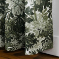 Photograph of fabric panel featuring a dark green and light green botanical pattern of leaves and flowers on a textured white background, draped over a wooden floor