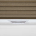 Close-up of a brown textured pleated cellular window Blind with a white bottom rail and an integrated white pull handle resting on a white window sill