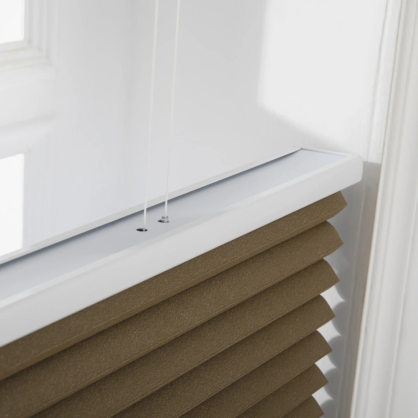 Photograph of a brown textured cellular window Blind with a white headrail and visible thin white control cords installed on a white window frame