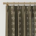 Olive green pinch pleat curtains with a repeating white stylized floral motif and subtle vertical pinstripes hanging from a polished gold curtain rod with matching rings