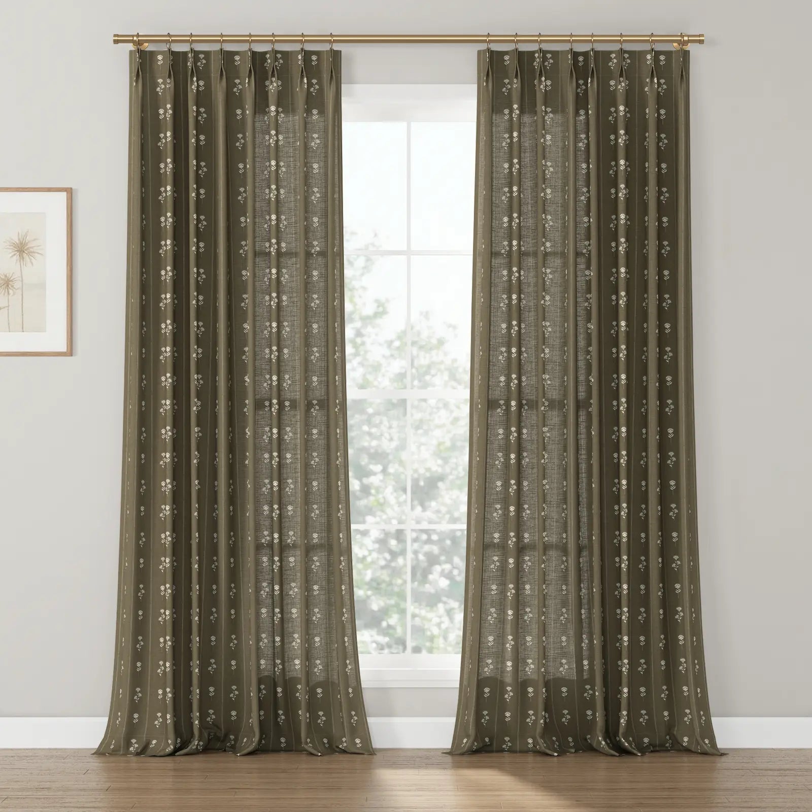 Dark olive-brown textured window curtains with a repeating white floral block print pattern, suspended from a brass rod, illuminating a room with light hardwood floors and a framed palm tree art print on the left wall