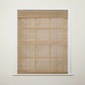 Photograph of an interior window featuring natural light tan woven wood blinds partially drawn down against an off-white wall with crisp white trim