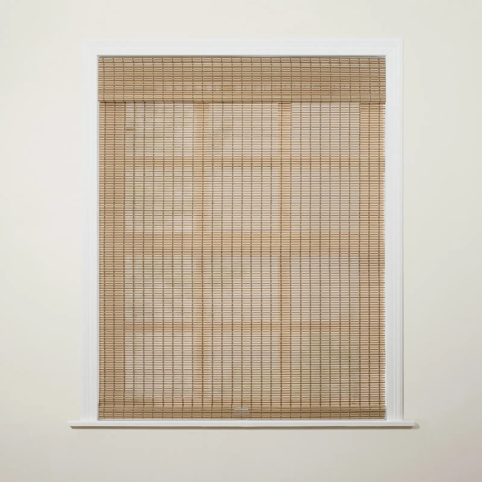 Photograph of an interior window featuring natural light tan woven wood blinds partially drawn down against an off-white wall with crisp white trim