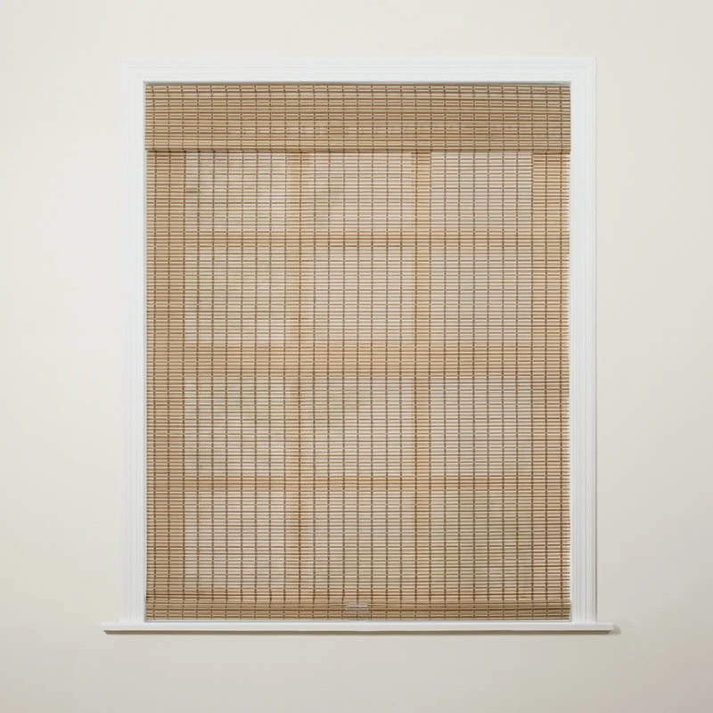 Photograph of an interior window featuring natural light tan woven wood blinds partially drawn down against an off-white wall with crisp white trim