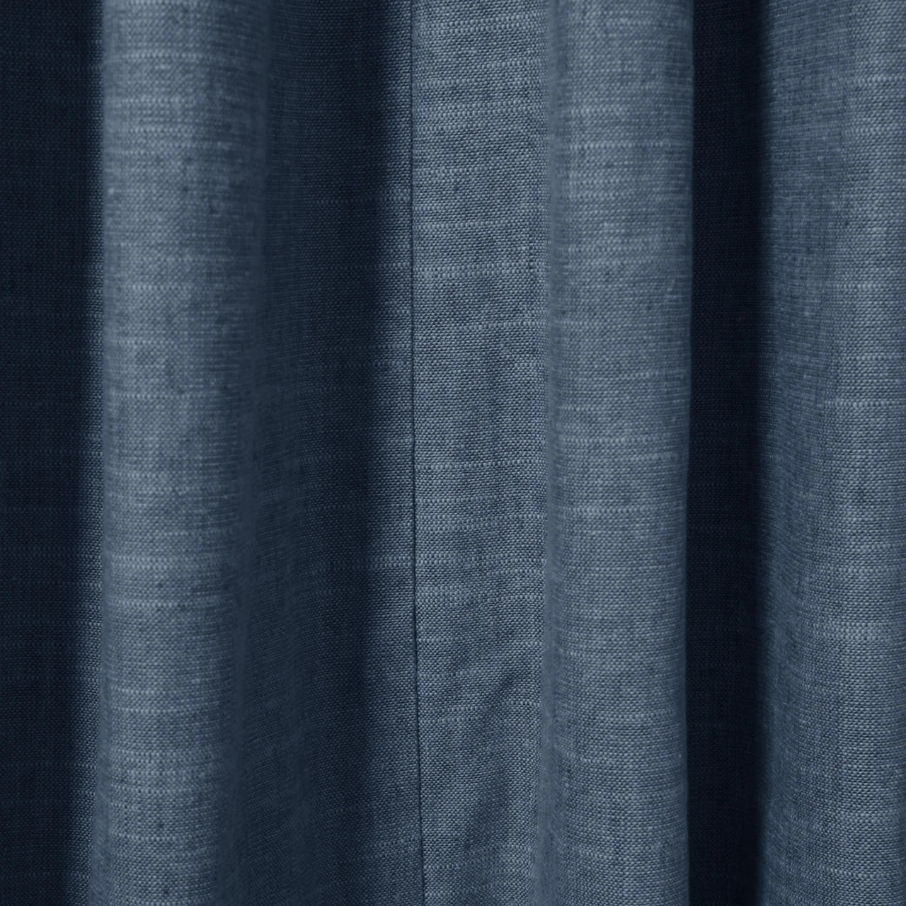 Muted indigo blue linen-like fabric with soft vertical folds, a distinctive central seam, and subtle heathered texture