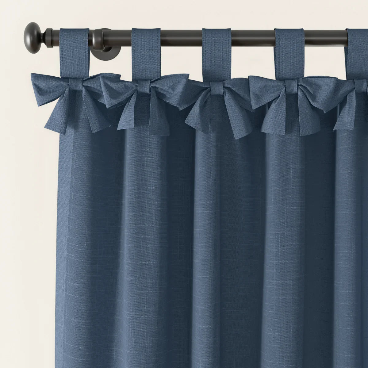 Textile product of textured denim blue curtains with decorative bow tie top loops hanging from a black rod