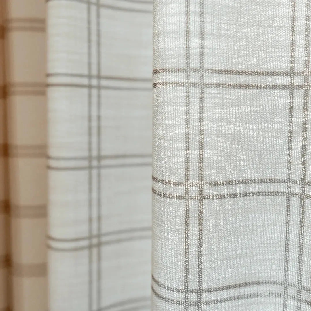 Close-up of light beige textured fabric curtain featuring a subtle brown grid pattern and soft vertical folds