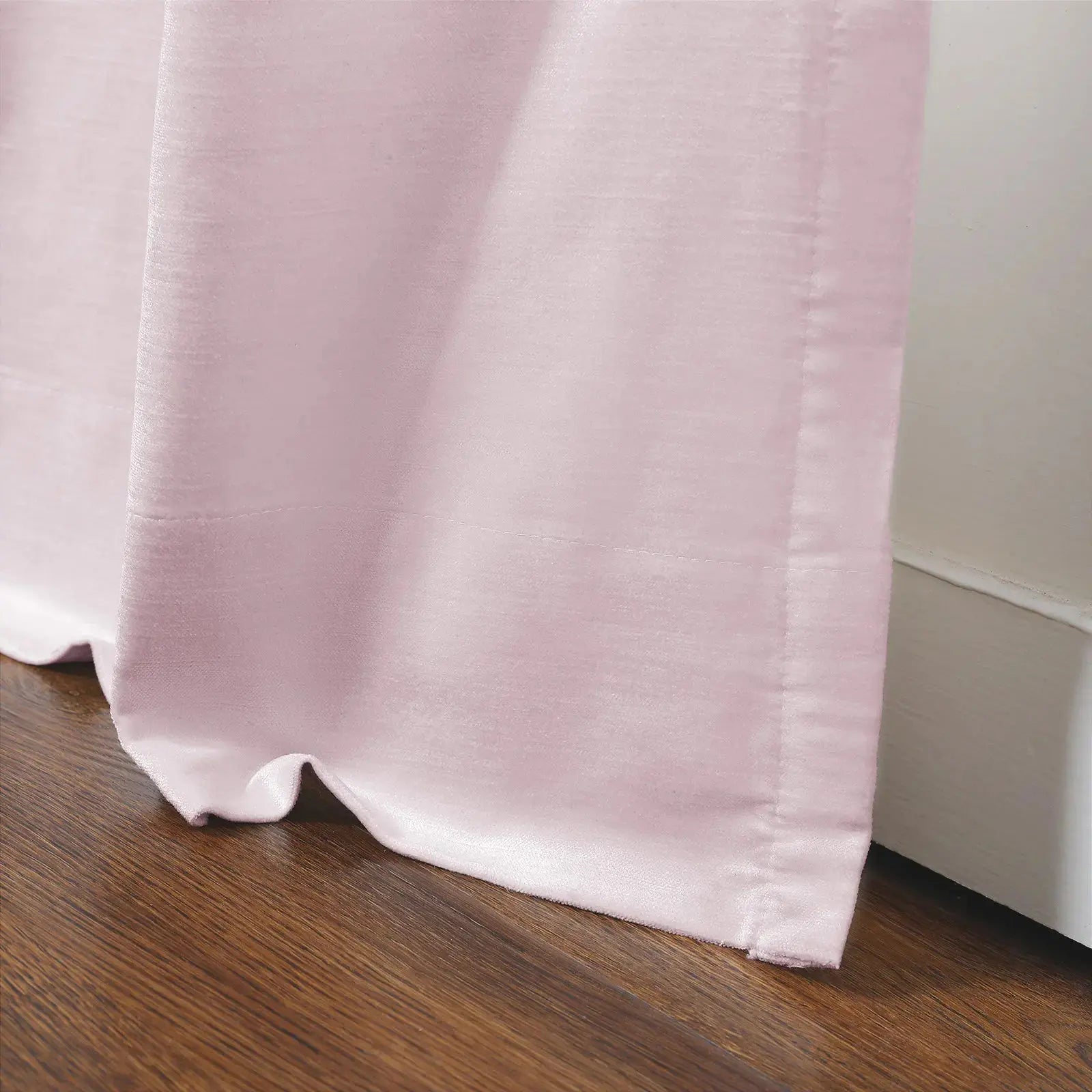 Photograph of a soft pink velvet curtain pooling slightly on a rich brown wooden floor against a white baseboard