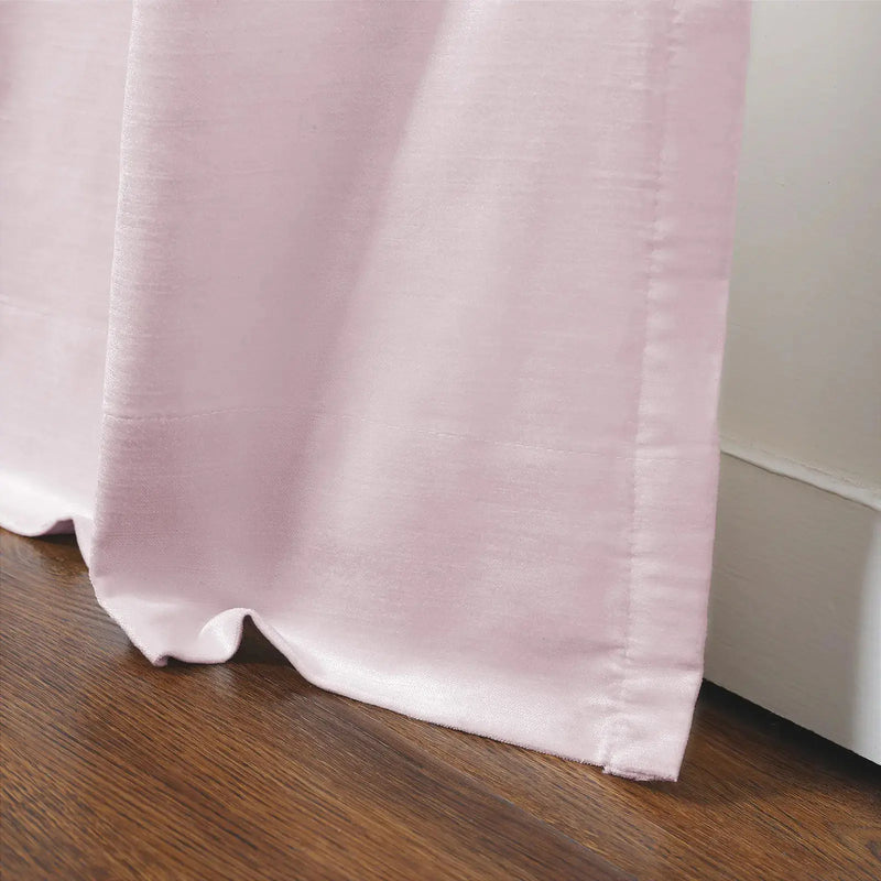 Photograph of a soft pink velvet curtain pooling slightly on a rich brown wooden floor against a white baseboard