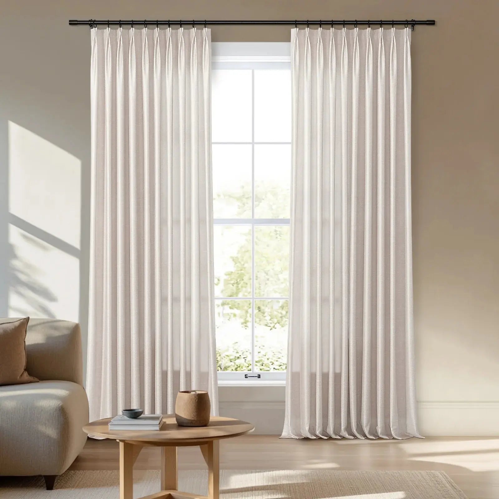 Creamy white ripple fold curtains on a black rod in a bright modern living room with a wooden coffee table and sunlit green foliage