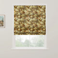A Roman blind with a dense botanical pattern in autumn greens and browns covers the upper window, revealing blurred trees outside and a framed rustic landscape painting on the adjacent wall