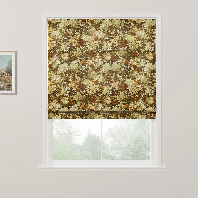 A Roman blind with a dense botanical pattern in autumn greens and browns covers the upper window, revealing blurred trees outside and a framed rustic landscape painting on the adjacent wall