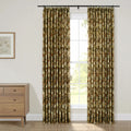 Photograph of a cozy room interior featuring pleated olive green and brown floral patterned curtains framing a window with white grid panes revealing green foliage outside, next to a mid-century modern wooden dresser and a framed botanical print on the wall